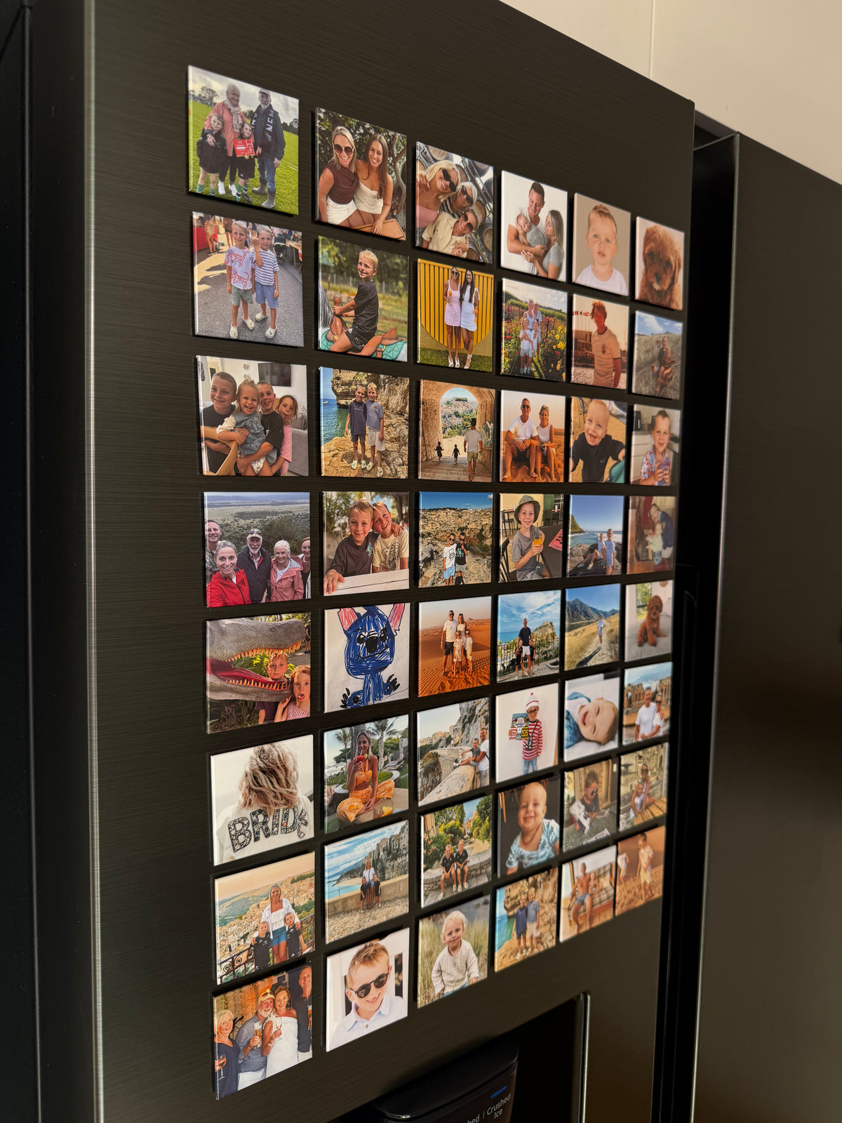 A black refrigerator door decorated with a grid of 5cm x 5cm personalised photo magnets
